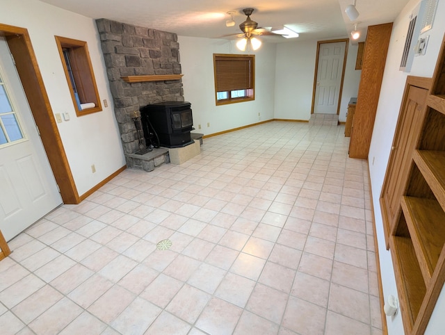 unfurnished living room featuring baseboards, a ceiling fan, a wood stove, and light tile patterned floors