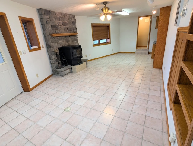 unfurnished living room with a ceiling fan, a wood stove, and light tile patterned flooring