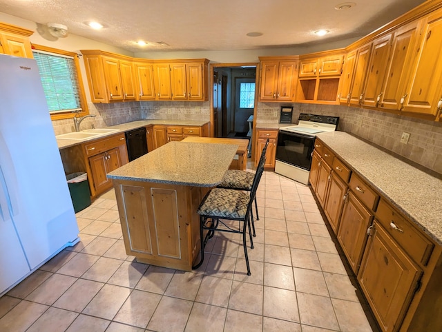 kitchen featuring a center island, a sink, dishwasher, range with electric cooktop, and freestanding refrigerator