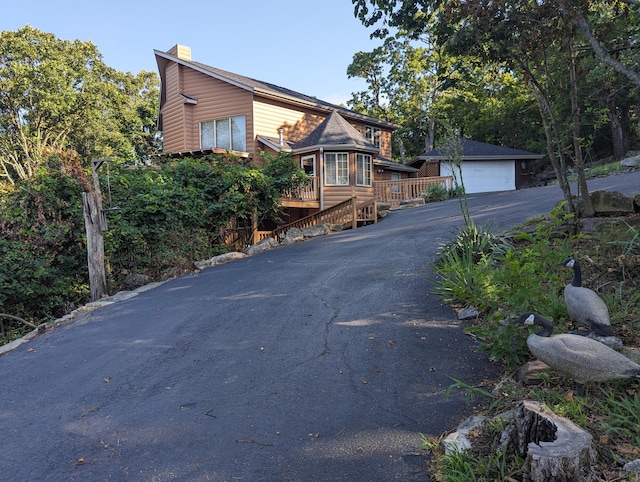 rustic home featuring faux log siding, driveway, a chimney, a garage, and an outdoor structure