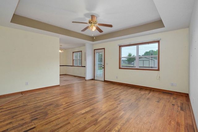 spare room featuring a raised ceiling, light hardwood / wood-style floors, and ceiling fan with notable chandelier