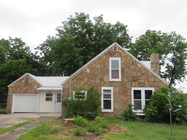 view of front of home with concrete driveway, an attached garage, a chimney, and stone siding