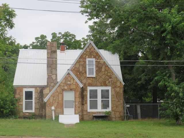 view of front of property featuring fence, a chimney, stone siding, and metal roof