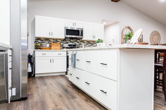 kitchen with wood finished floors, decorative backsplash, vaulted ceiling with beams, stainless steel appliances, and white cabinets