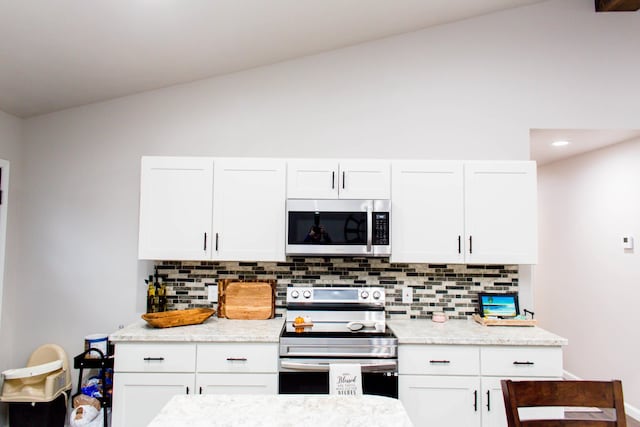 kitchen with stainless steel appliances, vaulted ceiling, white cabinetry, decorative backsplash, and light stone counters