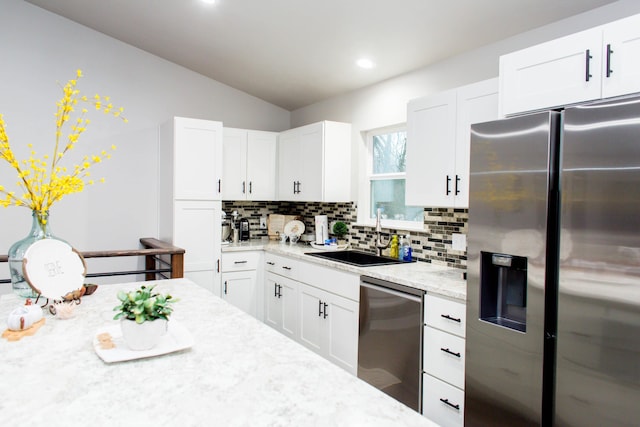 kitchen with stainless steel appliances, backsplash, vaulted ceiling, a sink, and light stone countertops