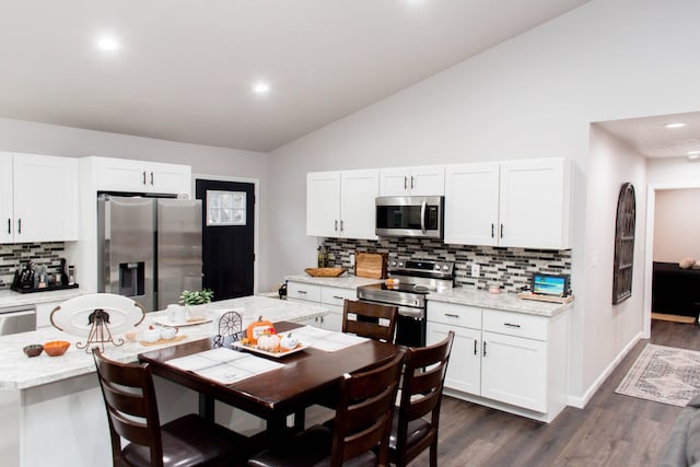 kitchen with stainless steel appliances, dark wood-style flooring, vaulted ceiling, white cabinetry, and decorative backsplash