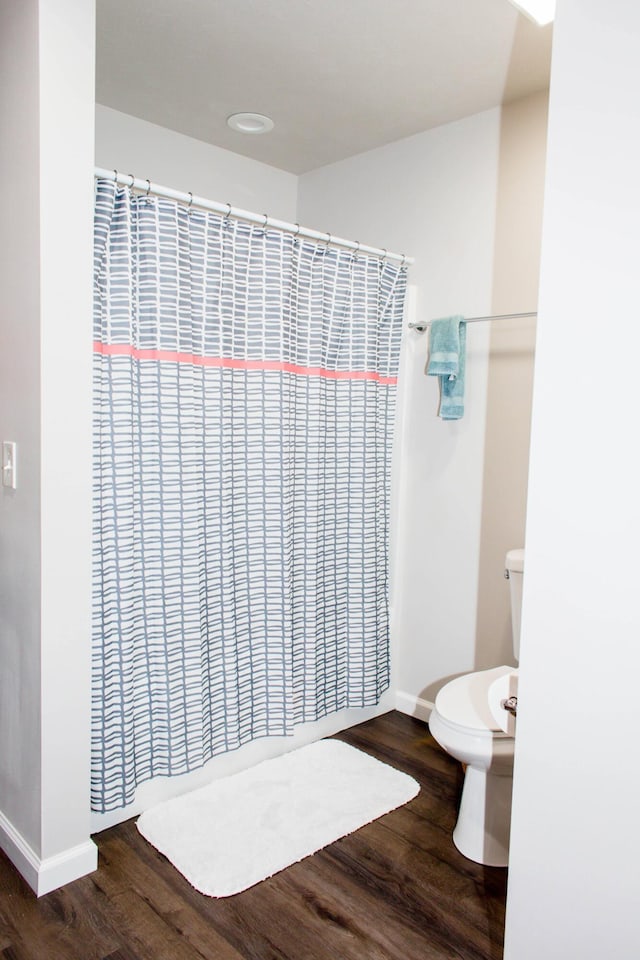 bathroom featuring baseboards, wood finished floors, and toilet