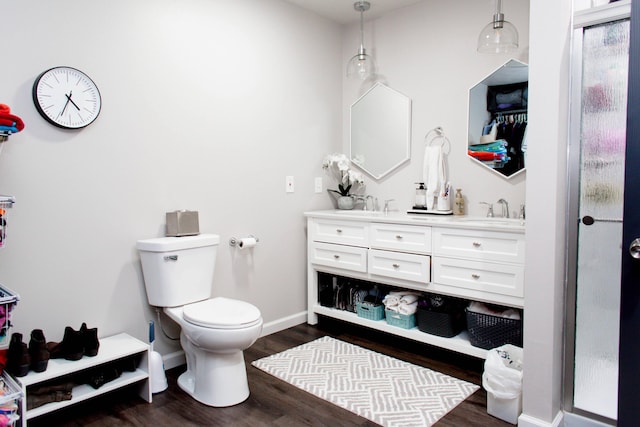 bathroom featuring double vanity, wood finished floors, toilet, a sink, and baseboards