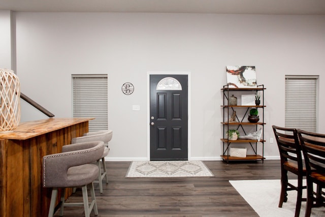 foyer with a dry bar, baseboards, and dark wood finished floors
