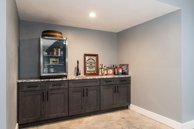 bar featuring dark brown cabinetry, light stone countertops, and sink