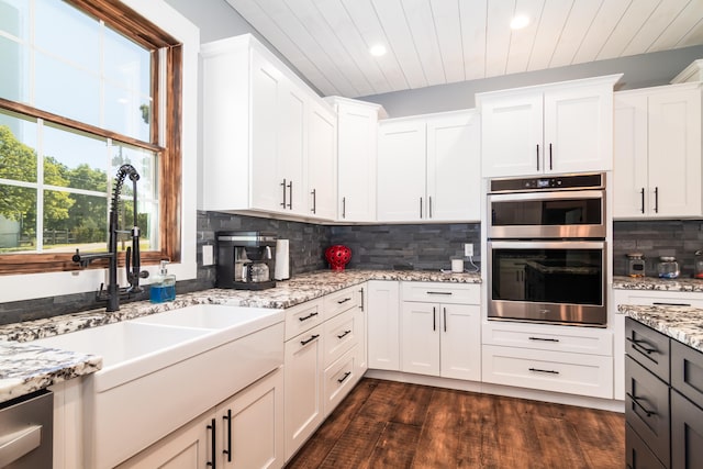 kitchen with dark hardwood / wood-style flooring, light stone counters, decorative backsplash, white cabinets, and appliances with stainless steel finishes