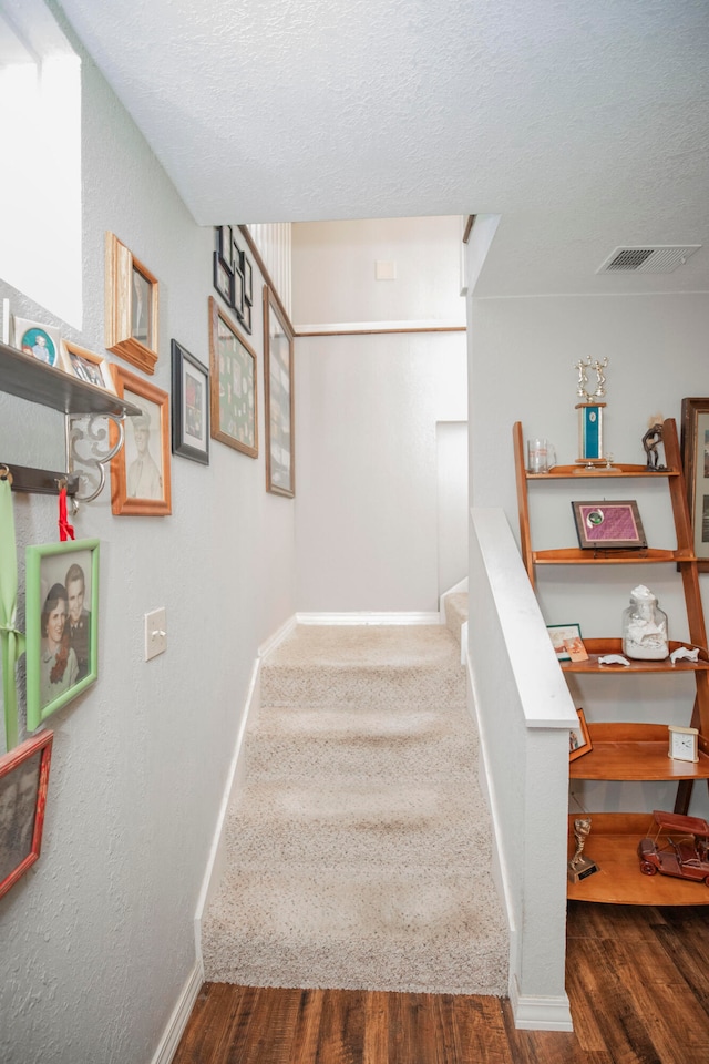 stairs with wood-type flooring and a textured ceiling