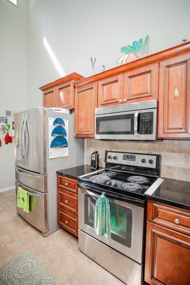 kitchen featuring appliances with stainless steel finishes, dark stone counters, decorative backsplash, and light tile patterned floors