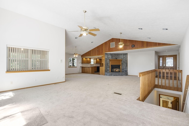 unfurnished living room with high vaulted ceiling, a fireplace, wood walls, and carpet