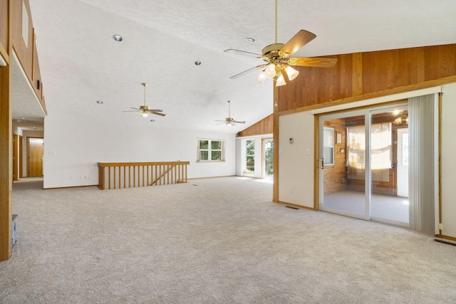 carpeted spare room with a textured ceiling, wood walls, and high vaulted ceiling