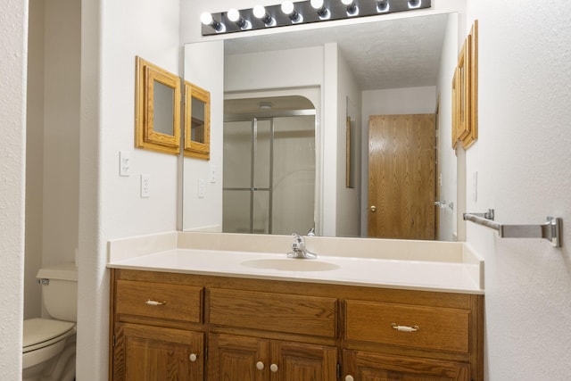 bathroom with vanity, a shower with door, toilet, and a textured ceiling