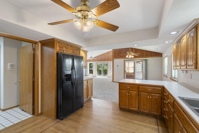 kitchen with pendant lighting, lofted ceiling, kitchen peninsula, black refrigerator with ice dispenser, and light hardwood / wood-style floors