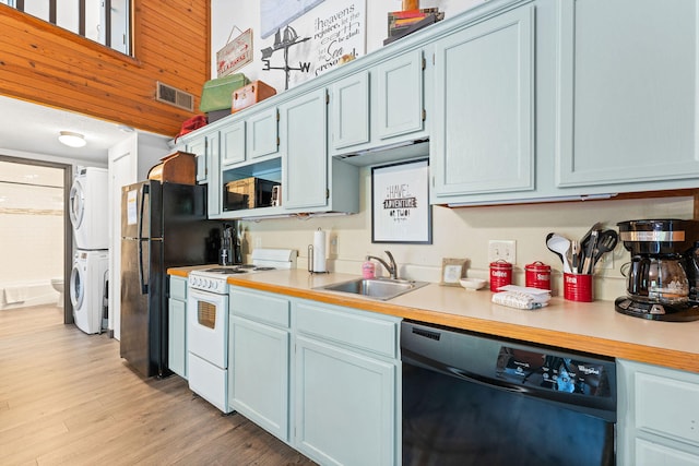 kitchen with light wood-type flooring, blue cabinetry, stacked washer / dryer, sink, and black appliances