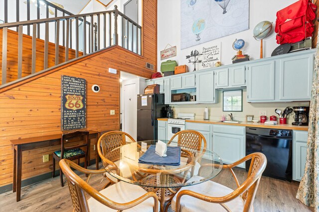 dining space with a towering ceiling, light hardwood / wood-style floors, sink, and wooden walls