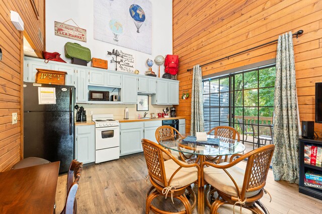 kitchen with a towering ceiling, black appliances, sink, and wooden walls