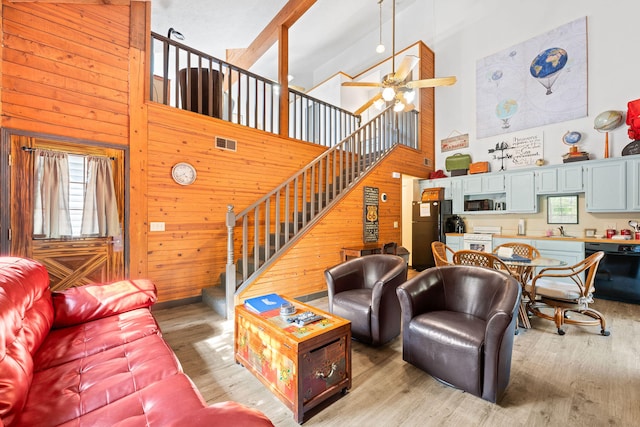 living room with sink, wood walls, light hardwood / wood-style floors, and high vaulted ceiling