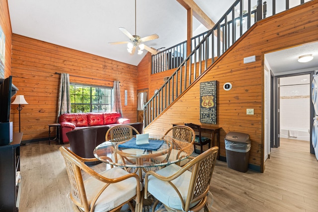 dining space featuring wooden walls, light wood-type flooring, and high vaulted ceiling