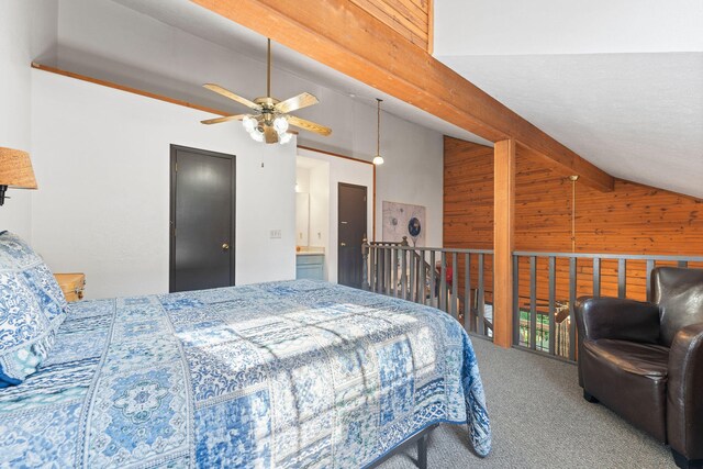 carpeted bedroom with ceiling fan, beam ceiling, wooden walls, high vaulted ceiling, and ensuite bath