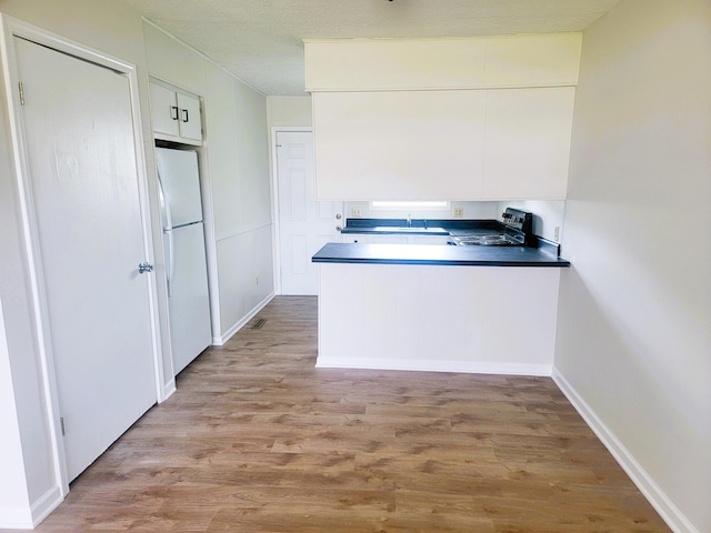 kitchen featuring light hardwood / wood-style flooring, white fridge, black range with electric cooktop, and white cabinetry