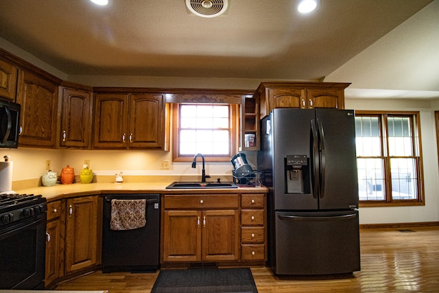 kitchen with lofted ceiling, light hardwood / wood-style floors, black appliances, and sink