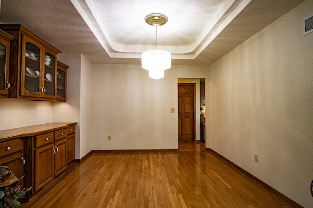 unfurnished dining area featuring a tray ceiling, a chandelier, and wood-type flooring