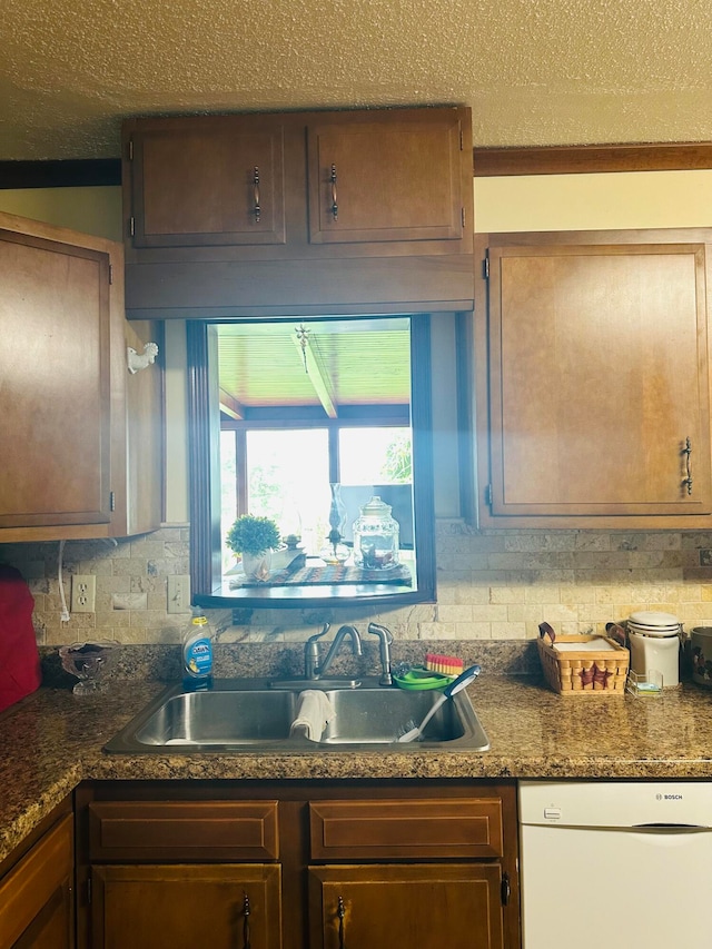 kitchen featuring white dishwasher, backsplash, sink, and a textured ceiling