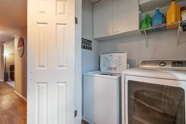 clothes washing area featuring a textured ceiling, light wood-type flooring, separate washer and dryer, and cabinets