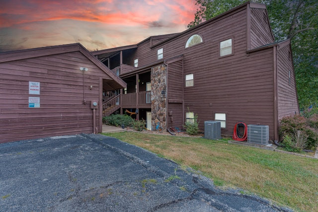 property exterior at dusk featuring a yard, a wooden deck, and cooling unit