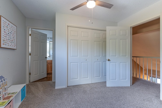 unfurnished bedroom with dark carpet, a textured ceiling, a closet, and ceiling fan