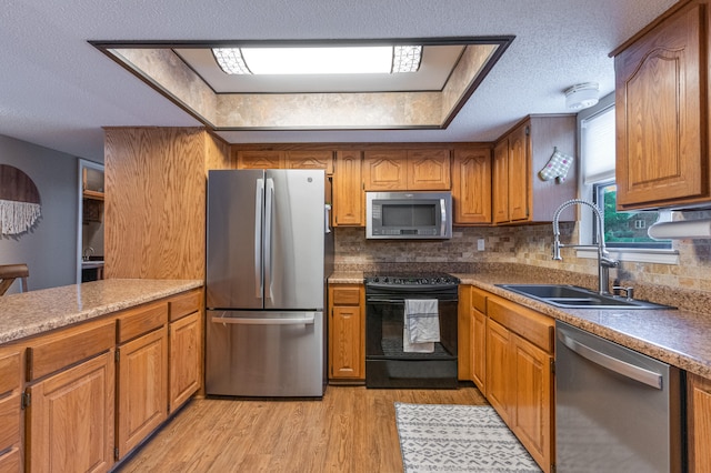 kitchen featuring sink, tasteful backsplash, a textured ceiling, appliances with stainless steel finishes, and light wood-type flooring