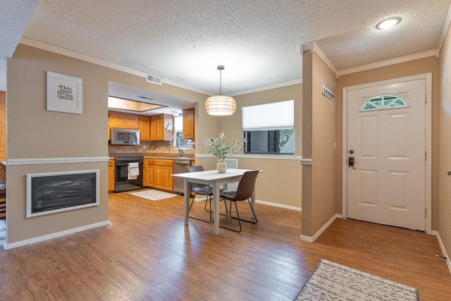 kitchen with stainless steel appliances, light hardwood / wood-style floors, pendant lighting, and ornamental molding