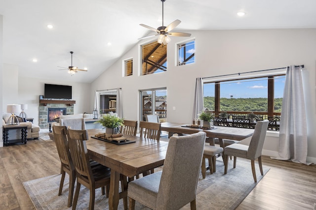 dining room featuring ceiling fan, a stone fireplace, light wood-type flooring, and high vaulted ceiling