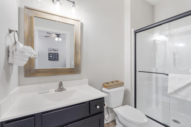 bathroom featuring ceiling fan, vanity, a shower with door, and toilet