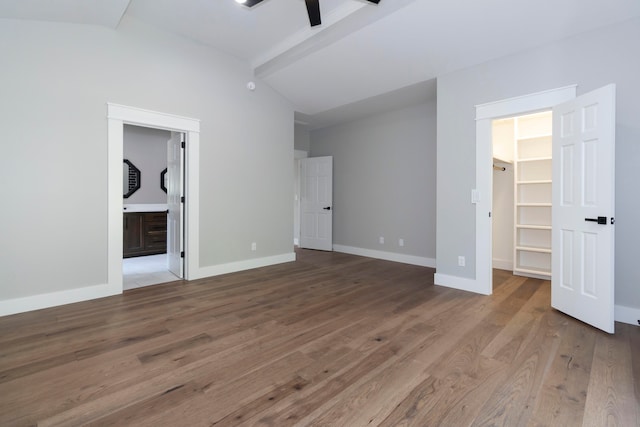 unfurnished bedroom featuring lofted ceiling with beams, a spacious closet, ceiling fan, hardwood / wood-style flooring, and connected bathroom