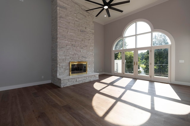 unfurnished living room featuring ceiling fan, a stone fireplace, dark hardwood / wood-style floors, a towering ceiling, and ornamental molding