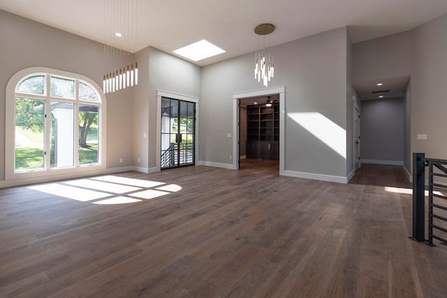 unfurnished living room with an inviting chandelier, a skylight, dark hardwood / wood-style flooring, and a wealth of natural light