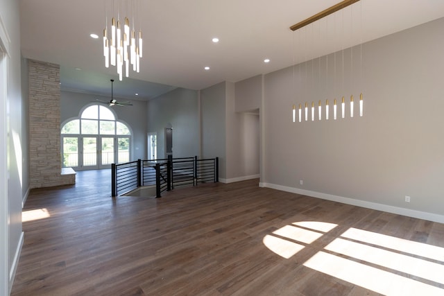 spare room featuring ceiling fan with notable chandelier, dark hardwood / wood-style floors, and a high ceiling