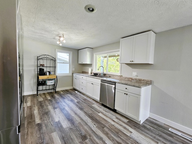 kitchen with hardwood / wood-style floors, sink, white cabinetry, appliances with stainless steel finishes, and a textured ceiling