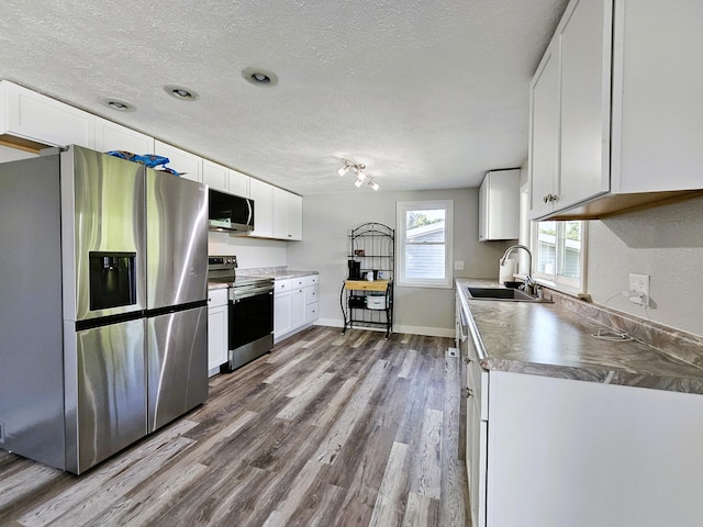 kitchen featuring hardwood / wood-style floors, stainless steel appliances, white cabinets, sink, and a textured ceiling