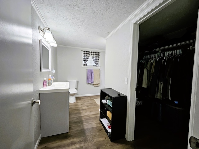 bathroom featuring vanity, wood-type flooring, a textured ceiling, crown molding, and toilet