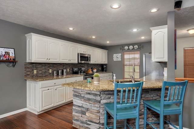 kitchen featuring white cabinets, dark wood-type flooring, appliances with stainless steel finishes, light stone countertops, and a kitchen bar