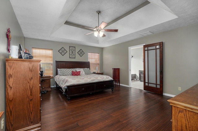 bedroom with a textured ceiling, ceiling fan, a tray ceiling, and dark hardwood / wood-style flooring