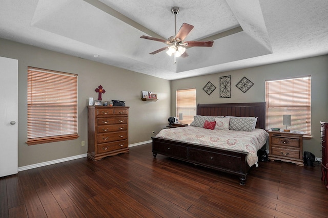 bedroom with dark wood-type flooring, a tray ceiling, multiple windows, and ceiling fan