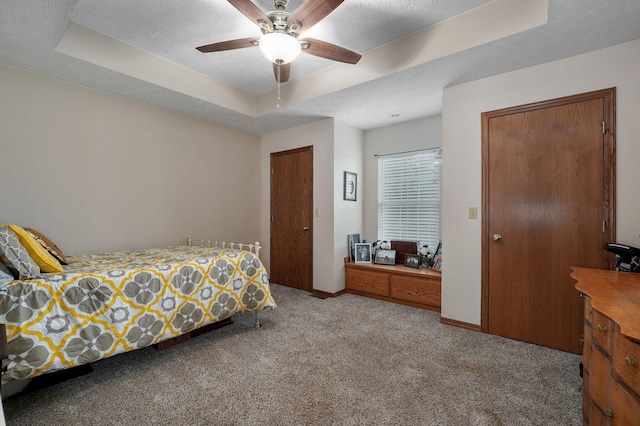 bedroom featuring light carpet, ceiling fan, a tray ceiling, and a textured ceiling